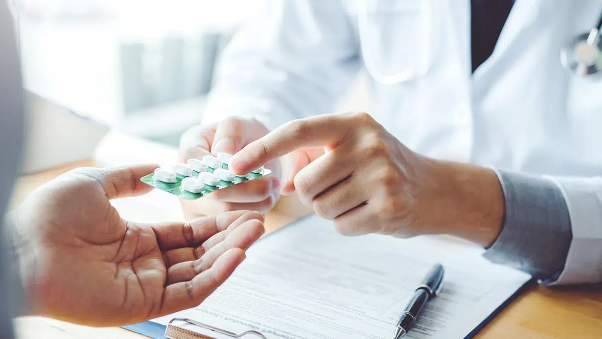 A doctor hands pills to a patient. Medication-assisted treatment for opioid addiction combines medication and therapy for recovery