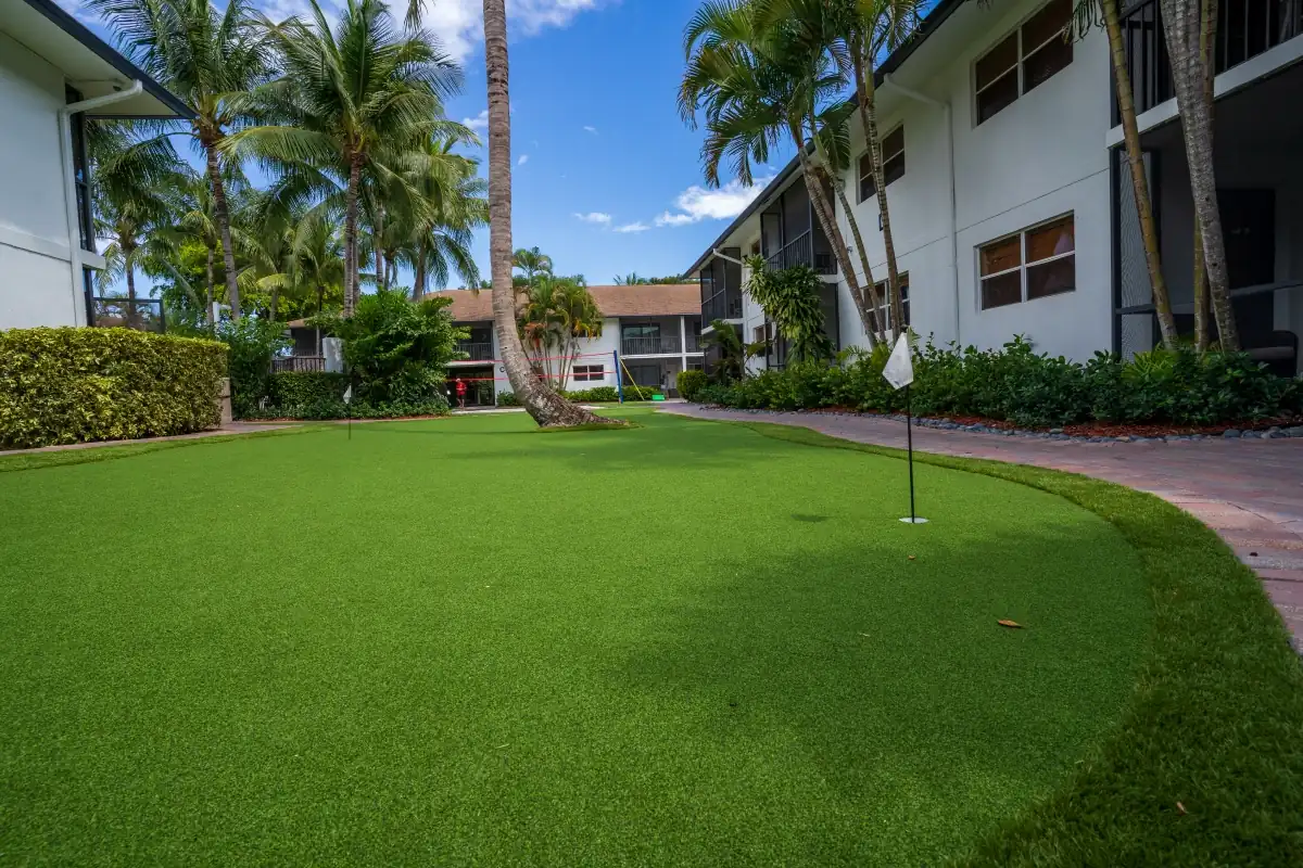 Outdoor recreation courtyard at The Recovery Team Delray Beach facility featuring a putting green, palm trees, and residential-style treatment buildings in a serene recovery environment
