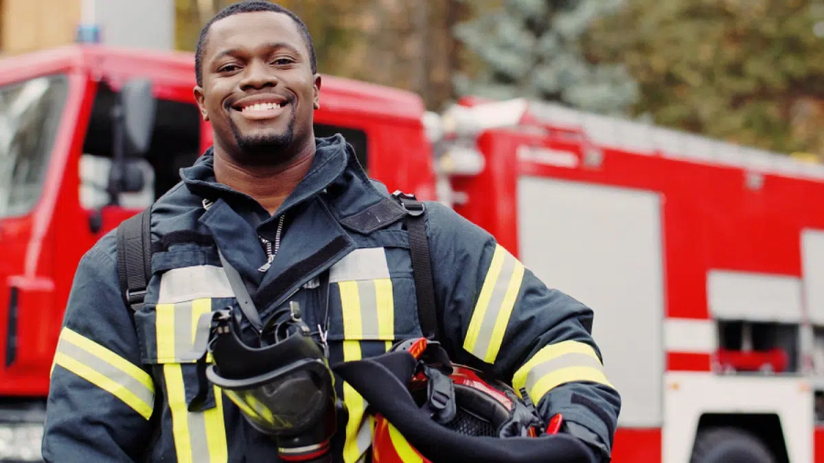 Firefighter smiling in front of a fire truck. Addressing addiction and mental disorders, like PTSD, is crucial for first responders.