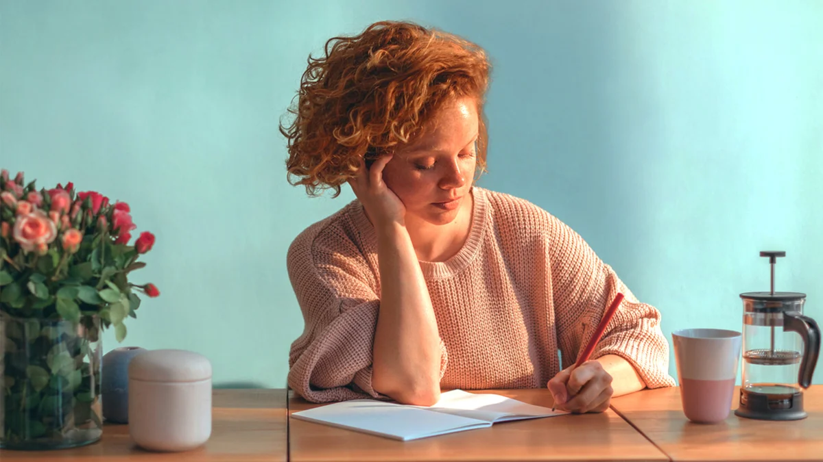 Woman writing at a desk and covered in sunlight from the window.