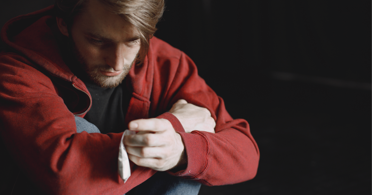 Man in a red hoodie holding his legs and a bag of cocaine.
