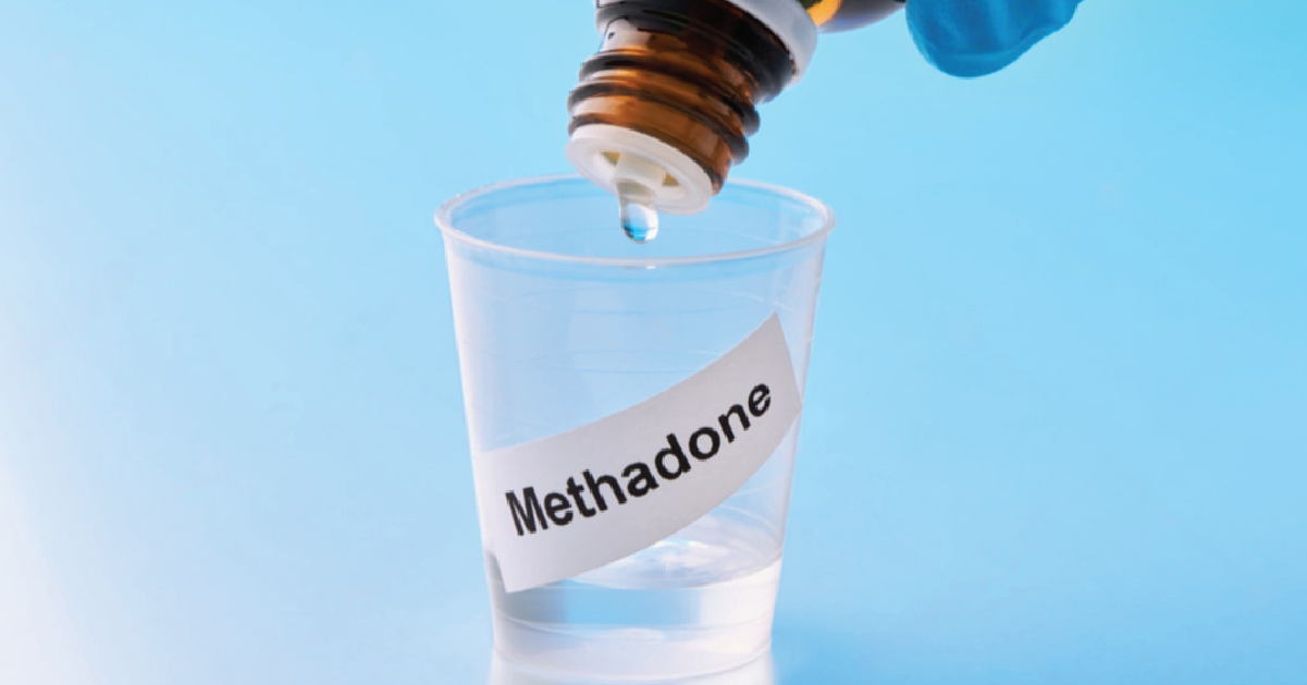 Clear cup labeled ‘methadone’ being filled with a clear liquid from a container.