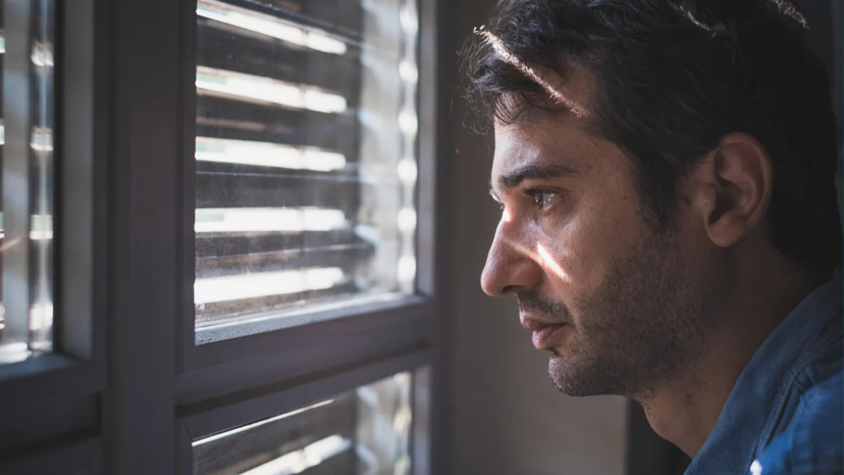 Man staring outside of window through blinds
