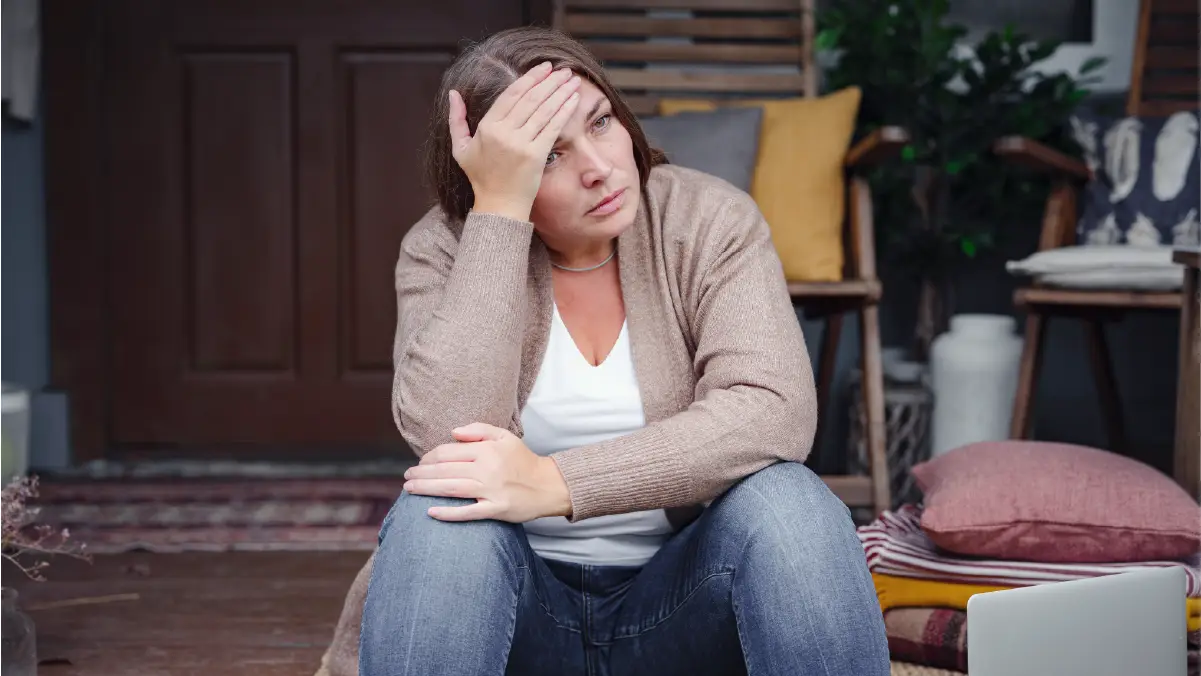 Woman sitting on a porch, holding her head in distress, symbolizing the challenges and barriers to accessing medication treatment.