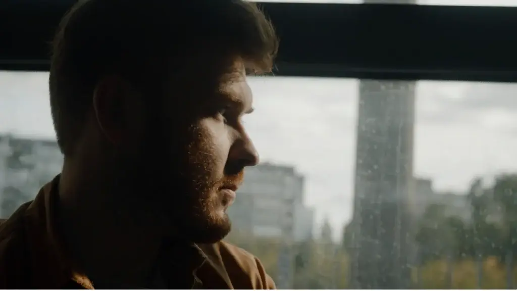 A man struggling with opioid addiction gazes out the window with a distant expression