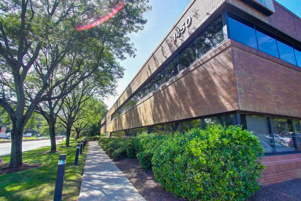 Exterior view of a modern brick office building surrounded by trees and landscaping on a sunny day