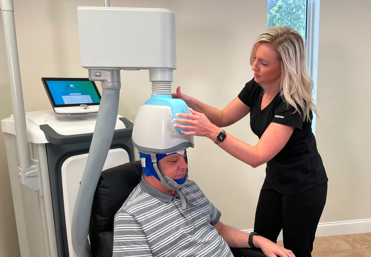 A woman in a white coat adjusts a transcranial magnetic stimulation (TMS) device on a man's head.