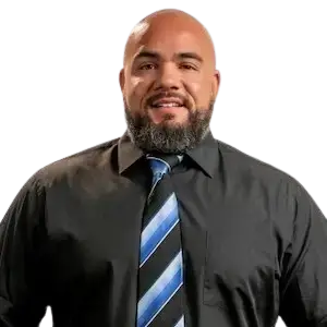A man with a shaved head and beard, wearing a suit and striped tie, smiles at the camera.