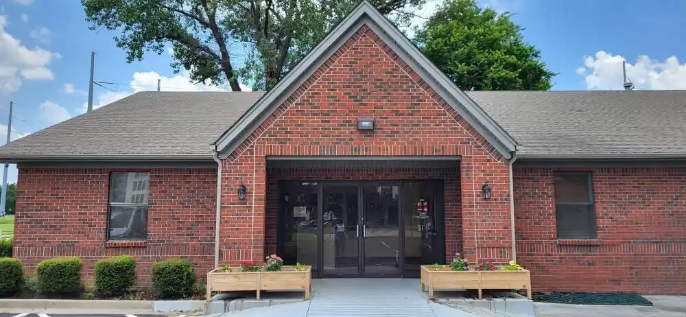 Exterior entrance of The Recovery Team facility in North Little Rock, Arkansas, featuring a brick building with double glass doors and landscaped planters.